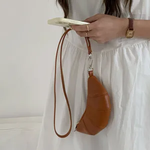 Primo piano di una mini borsa croissant marrone vintage indossata al collo, accessorio chic.