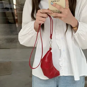 Primo piano di un elegante portamonete a croissant rosso sospeso alle mani, chic.