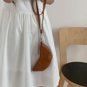 Primo piano di un mini borsellino a forma di croissant marrone, dettaglio di accessorio chic.