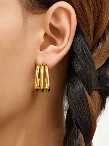 Primer plano detallado de pendientes de aro cuadrados multicapa chapados en oro.