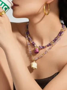 Nahaufnahme der mehrlagigen Kristall- und Rosen-Halskette mit goldenen Creolen und Details.