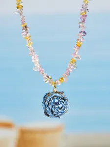 Detailaufnahme des blauen Harzrosenanhängers mit bunten Kristallsplittern am Strand.