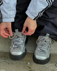 Close-up detail view of metallic beaded bow shoelace charms attached to stylish sneakers.