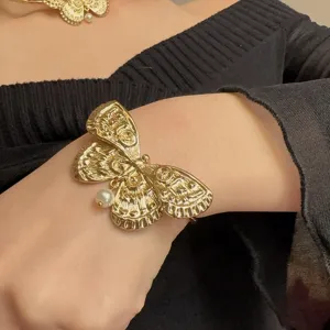Gedetailleerd overzicht van gouden vlinderarmband met parelhanger, elegant retro modesieraad.