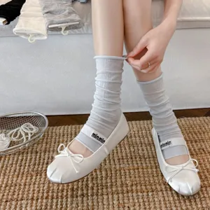 Nahaufnahme von sommerlichen, transparenten grauen Stulpen kombiniert mit weißen Ballerinas.