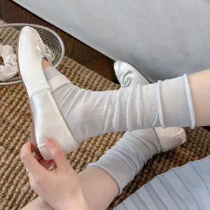 Nahaufnahme von weißen Satin-Ballerinas kombiniert mit transparenten grauen Socken.