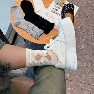 Detail view of hollow out bow mid calf socks paired with white sneakers for sweet daily look