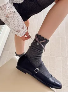 Nahaufnahme von grauen Slouch-Socken mit eleganten Schleifenbändern und kleinem Knopf.