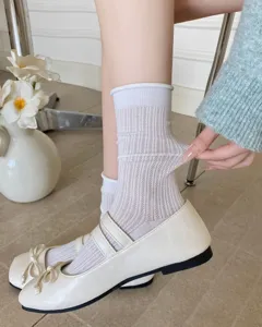 Nahaufnahme von transparenten Mesh-Mittelsocken mit Rollrand und weißen Mary Jane Flachschuhen.