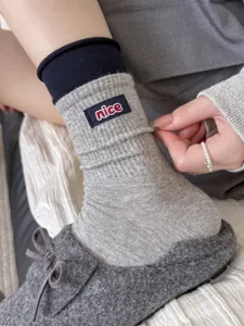 Close-up of women's cozy grey ribbed slouch socks with a cute embroidered nice label detail.