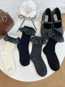 Vue détaillée de chaussettes en tricot à volants et manchette écossaise sur table blanche.