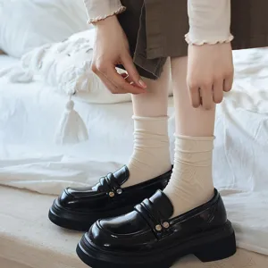 Women's black platform chunky loafers paired with beige knit crew socks, retro casual style.