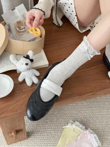 Close-up detail of white lace ruffle mid-calf mesh socks paired with classic black flats.