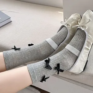 Detailed shot of women's grey ribbed mid-tube socks featuring cute black bows, paired with white flats.