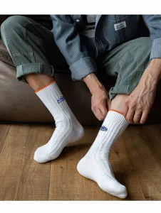 Detailansicht weißer Herren-Rippsocken mit orangefarbenem Rand und gesticktem Logo-Design.