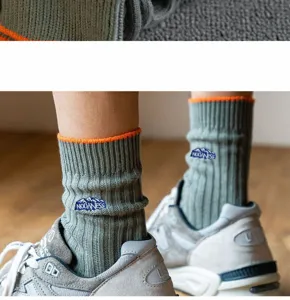 Detailaufnahme der grünen Rippenstrümpfe mit orangem Bündchen und gesticktem Berglogo.