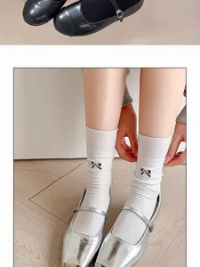 Nahaufnahme von weißen Wadenstrümpfen mit Schleifenstickerei und schicken silbernen Schuhen.
