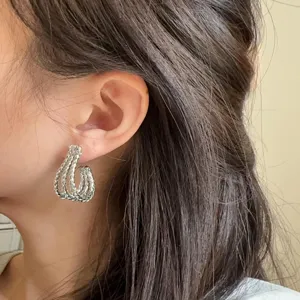 Detail close-up view of stylish silver J-shaped braided metal hoop earrings worn on ear.
