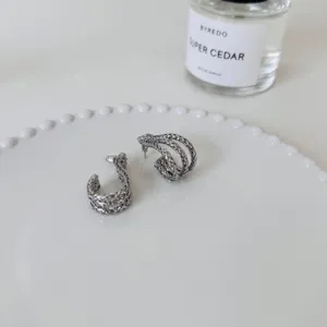 Detail view of trendy silver metal layered woven J-shaped earrings with sterling silver pins.