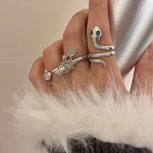 Vista detallada de anillos abiertos de metal de dragón y serpiente con pedrería brillante en la mano.