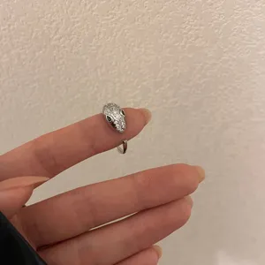 Primer plano detallado de un elegante anillo abierto en forma de serpiente con piedras brillantes.
