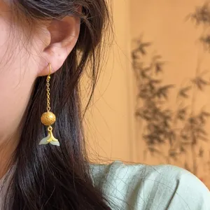 Detailed shot of Chinese style vintage gold tassel earrings with jade fish tail pendant.