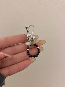 Detail shot of unique Y2K silver teapot sculpture ring with black beaded elastic band.