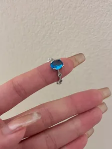 Detail view of a silver ring with an oval blue stone and delicate diamond accents on a finger.
