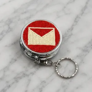 Porte-clés pilulier en métal perlé avec motif d'enveloppe rouge et blanche pour design portable.