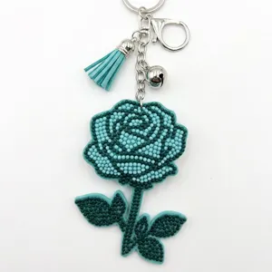 Gros plan détail de porte-clés rose en perles bleu canard avec pompon et clochette métal.