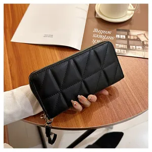 Black quilted long wallet for women with zipper closure and wrist strap, detail view on wooden table.