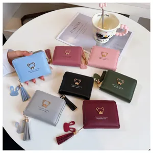 Close-up detail of cute short women wallet with bear emblem, tassel pendant and zip closure.