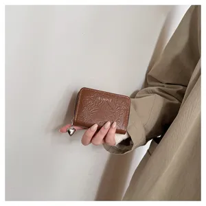 Close-up detail of compact brown wallet with cute heart charm and zipper closure.