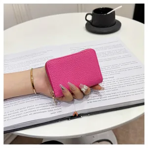 Primer plano detallado del tarjetero con cremallera de cuero rosa sobre libro.