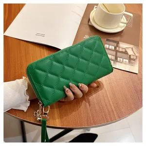 Detail shot of green quilted long wallet with zipper and wrist strap on wooden tabletop.