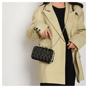 Dettaglio di pochette da sera intrecciata nera con manico in metallo e tracolla a catena.