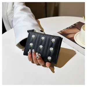 Close-up of black short folding wallet with cute white flower embroidery and zipper detail.