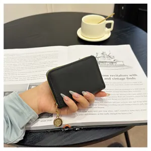 Close-up of a sleek black leather card holder with gold zipper and chic pendant detail.