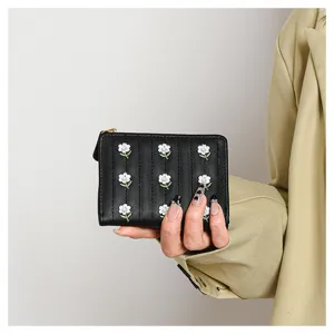 Detailed view of a chic black short wallet featuring delicate white floral embroidery and a zipper.