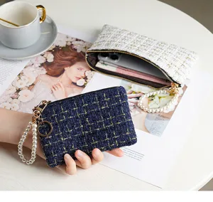 Detailed view of elegant tweed zipper coin pouch wallet with pearl wrist strap on chic desk setup.