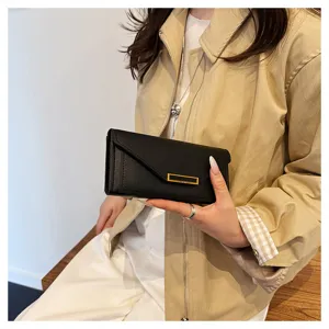 Close-up detail of a sleek black envelope long wallet held by a model with gold clasp.