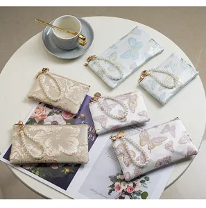Detailed view of Chinese style embroidered butterfly and floral zip coin purses with pearl straps on table.