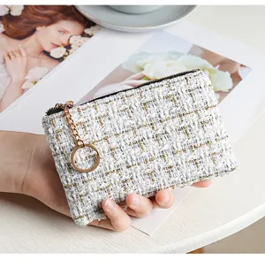 Detail shot of white tweed coin purse with gold zipper and key ring, stylish fabric texture.