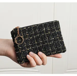 Detailed close-up view of black and gold tweed coin purse with zipper and metal key ring.