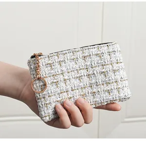Tweed coin purse detail showing white and black woven fabric texture with gold zipper and ring.