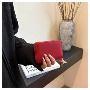 Red leather card holder detail shot with zipper closure and metal charm pendant showcase.
