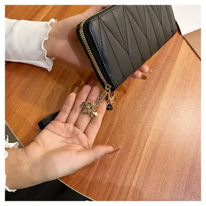 Detail view of black quilted long wallet with gold zipper and clover charm on wooden desk.