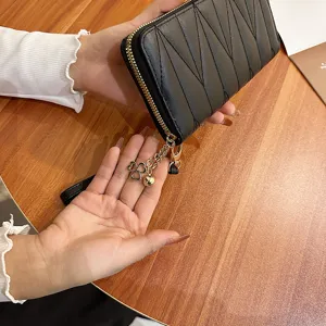 Black quilted long wallet for women with zip-around closure and chic clover charm pendant.