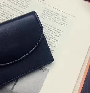 Close-up detail view of a minimalist dark PU leather card holder with flap and neat stitching.