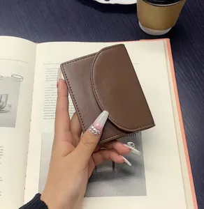 Detail view of a compact brown PU leather wallet held in hand, featuring a stylish flap design.